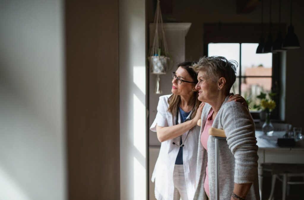 Healthcare worker or caregiver visiting senior woman indoors at home, helping her to walk.