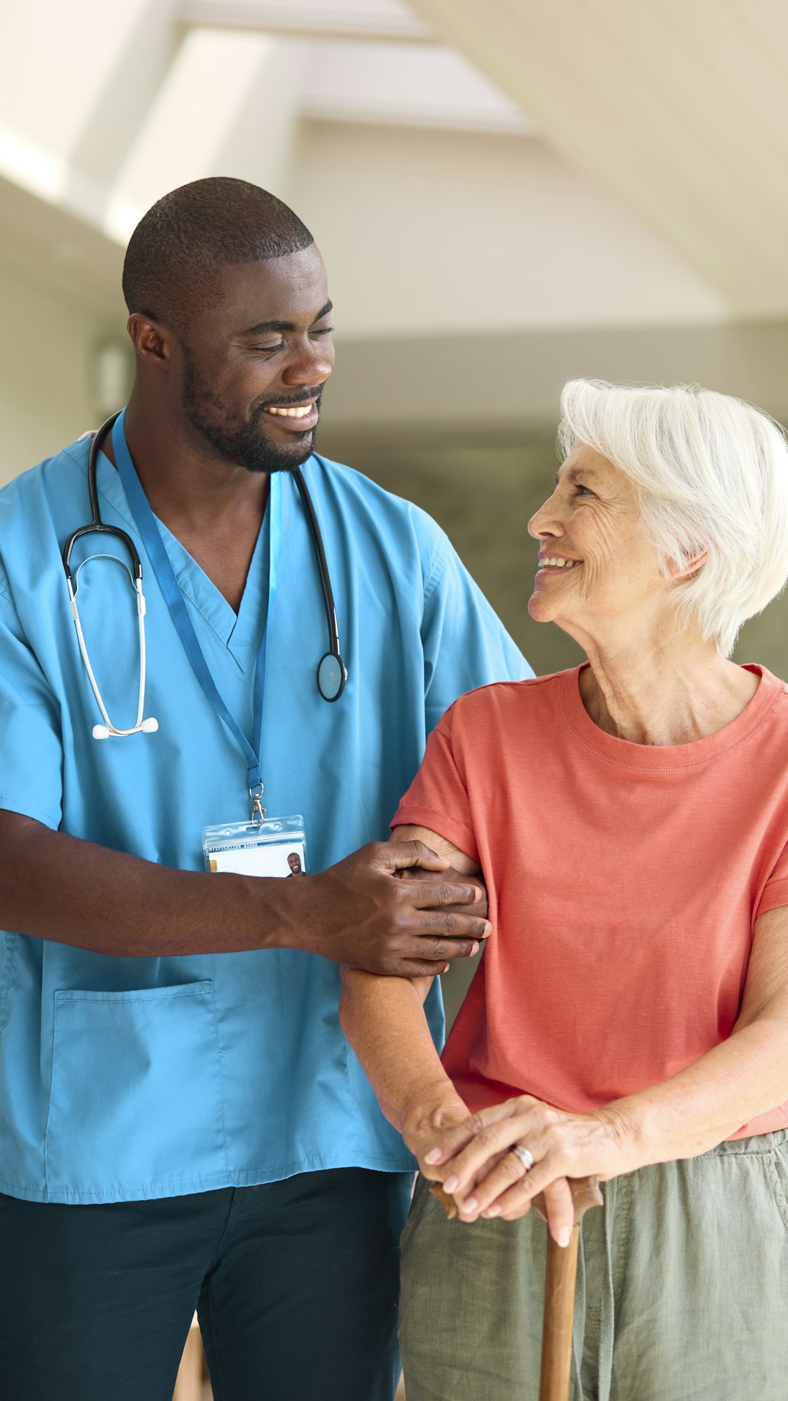 Male Nurse Visiting Senior Woman Using Walking Stick With Mobility Issues At Home