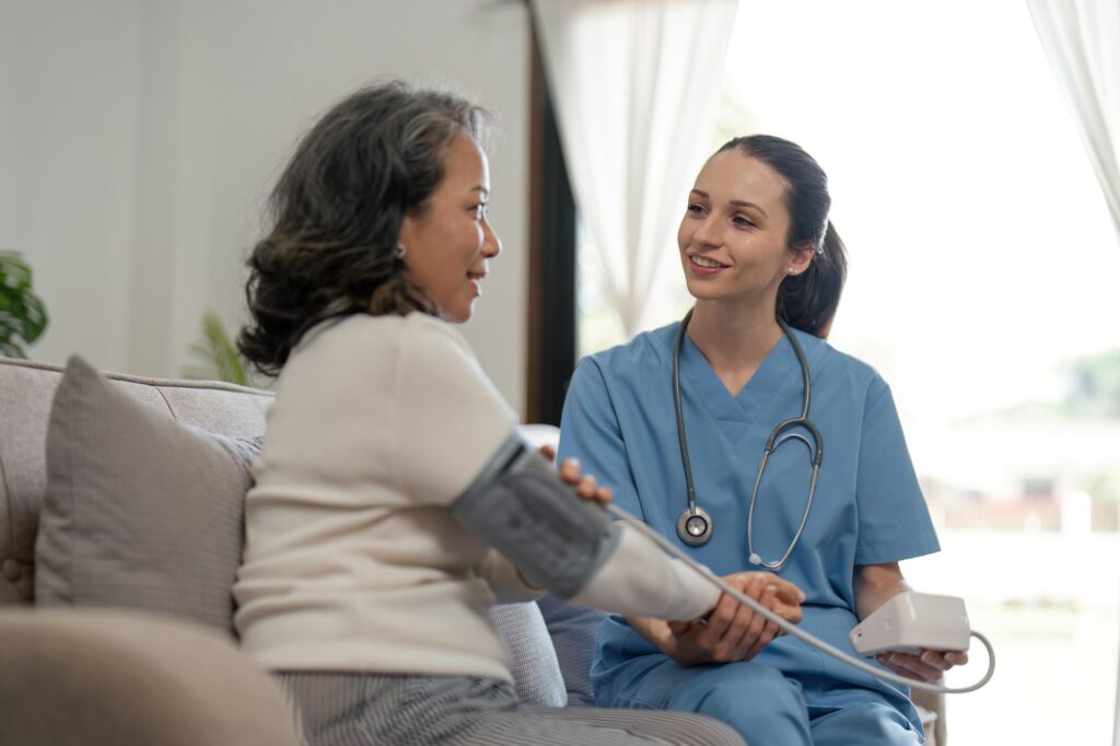 nurse doctor using digital tonometer check blood pressure for old asia female at home in elderly